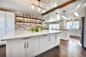 Kitchen with white cabinetry, hanging light fixtures, beamed ceiling, and a kitchen island