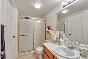 Bathroom featuring vanity, toilet, a shower with door, and tile flooring