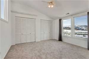 Unfurnished bedroom featuring light carpet, vaulted ceiling, ceiling fan, and two closets