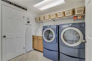 Clothes washing area with cabinets, washer and clothes dryer, and light tile floors