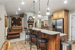 Kitchen with a kitchen bar, stainless steel refrigerator with ice dispenser, vaulted ceiling, decorative light fixtures, and light tile floors