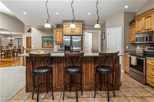 Kitchen with a kitchen island, hanging light fixtures, vaulted ceiling, appliances with stainless steel finishes, and light colored carpet