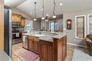 Kitchen with light tile floors, ceiling fan, appliances with stainless steel finishes, sink, and an island with sink