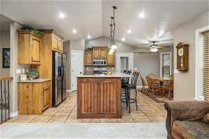 Kitchen featuring vaulted ceiling, light tile floors, stainless steel appliances, ceiling fan, and decorative light fixtures
