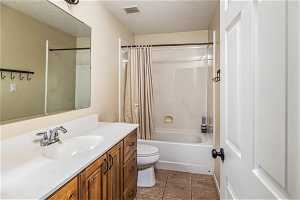 Full bathroom with vanity, shower / bath combo, a textured ceiling, toilet, and tile floors