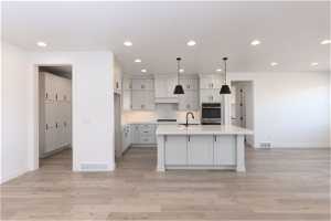 Kitchen featuring light wood-type flooring, stainless steel oven, backsplash, an island with sink, and sink
