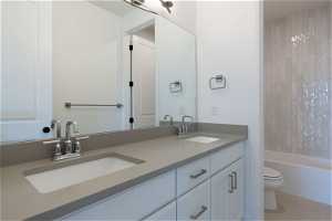 Full bathroom with tile flooring, toilet, tiled shower / bath, vanity with extensive cabinet space, and double sink