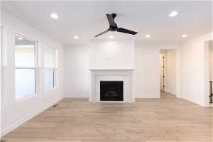 Unfurnished living room with a tiled fireplace, light hardwood / wood-style flooring, and ceiling fan