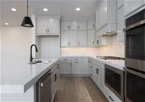 Kitchen with backsplash, light wood-type flooring, sink, stainless steel appliances, and pendant lighting