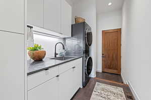 Washroom featuring estacked washer and dryer, cabinet space, dark wood-style floors, baseboards, and recessed lighting