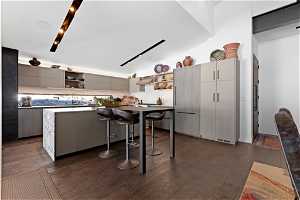 Kitchen featuring vaulted ceiling, a kitchen breakfast bar, range hood, tasteful backsplash, and dark wood-type flooring