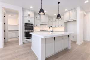 Kitchen with a center island with sink, tasteful backsplash, decorative light fixtures, and light hardwood / wood-style floors
