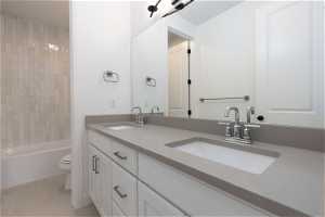 Full bathroom with tiled shower / bath combo, tile flooring, dual vanity, and toilet