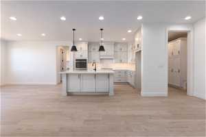 Kitchen with oven, a center island with sink, white cabinets, and light hardwood / wood-style floors