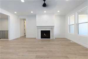 Unfurnished living room featuring a fireplace, light hardwood / wood-style floors, and ceiling fan
