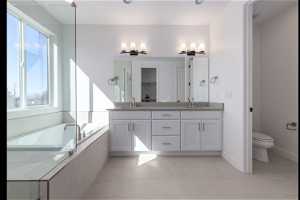 Bathroom featuring a wealth of natural light, tiled tub, double sink vanity, and tile floors