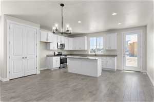 Kitchen featuring a kitchen island, stainless steel appliances, white cabinets, decorative light fixtures, and wood-type flooring
