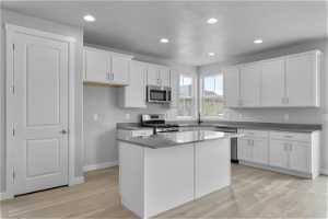 Kitchen with light hardwood / wood-style floors, white cabinetry, a kitchen island, stainless steel appliances, and sink