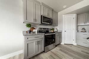 Kitchen featuring gray cabinets, stainless steel appliances, light stone counters, and light wood-type flooring