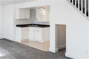 Basement Kitchen with white cabinetry, sink, and light colored carpet