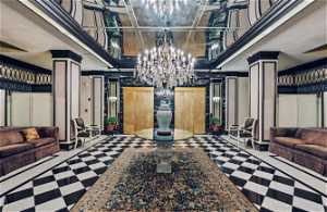 Foyer welcomes all with its black and white harlequin marble flooring, large crystal chandelier against mirrored ceilings and walls with the gold accents of the elevator doors.