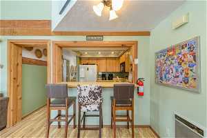 Kitchen with a kitchen breakfast bar, white fridge with ice dispenser, light hardwood / wood-style floors, and kitchen peninsula