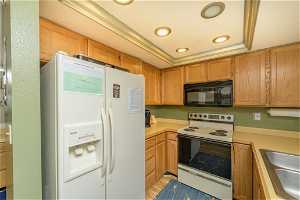 Kitchen with a tray ceiling, white appliances, light hardwood / wood-style floors, and sink