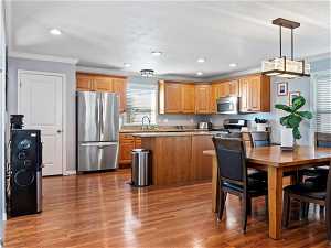 Kitchen featuring hardwood / wood-style floors, hanging light fixtures, appliances with stainless steel finishes, light stone counters, and crown molding
