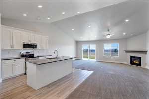 Kitchen with white cabinetry, sink, stainless steel appliances, and light carpet