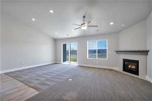 Unfurnished living room featuring a tile fireplace, light colored carpet, vaulted ceiling, and ceiling fan