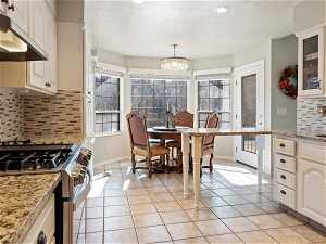 Kitchen featuring a notable chandelier, white cabinets, backsplash, gas range oven, and light stone countertops