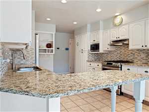 Kitchen with white cabinetry, sink, tasteful backsplash, stainless steel appliances, and light stone countertops