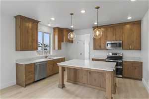 Kitchen with appliances with stainless steel finishes, sink, light hardwood / wood-style flooring, pendant lighting, and a center island