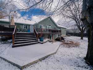 Snow covered back of property with a wooden deck