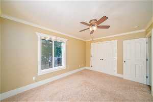 Unfurnished bedroom featuring light carpet, a closet, crown molding, and ceiling fan