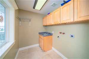 Laundry room with light tile flooring, electric dryer hookup, cabinets, and sink