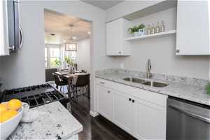 Kitchen featuring sink, dark wood-type flooring, appliances with stainless steel finishes, decorative light fixtures, and white cabinetry