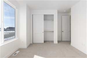 Unfurnished bedroom featuring multiple windows, light carpet, and a closet