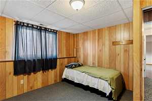 Carpeted bedroom with a paneled ceiling and wooden walls