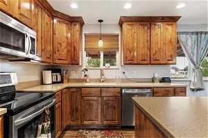 Kitchen with appliances with stainless steel finishes, decorative light fixtures, sink, and light stone counters