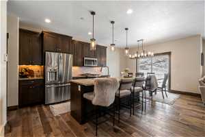 Kitchen featuring tasteful backsplash, appliances with stainless steel finishes, a chandelier, dark wood-type flooring, and decorative light fixtures
