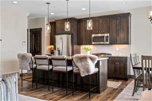 Kitchen with a breakfast bar, dark brown cabinetry, hanging light fixtures, dark hardwood / wood-style flooring, and appliances with stainless steel finishes