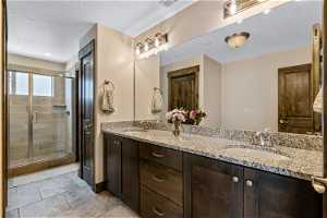 Bathroom featuring a textured ceiling, a shower with shower door, oversized vanity, tile flooring, and double sink