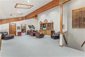 Carpeted living room featuring lofted ceiling with beams, a textured ceiling, and ceiling fan