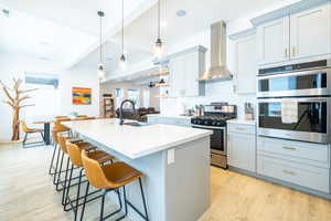 Kitchen with sink, wall chimney exhaust hood, appliances with stainless steel finishes, a center island with sink, and light hardwood / wood-style floors