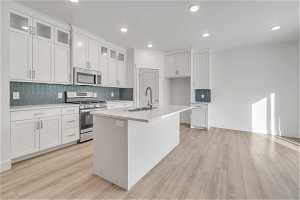 Kitchen featuring a kitchen island with sink, white cabinetry, sink, light hardwood / wood-style floors, and appliances with stainless steel finishes