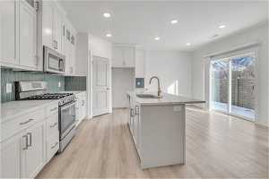 Kitchen featuring stainless steel appliances, sink, white cabinetry, and an island with sink