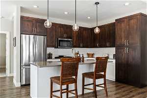 Kitchen featuring dark hardwood cabinets, tasteful backsplash, center island with sink, and stainless steel appliances.