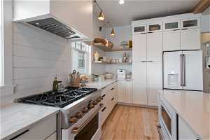 Kitchen with white cabinets, hanging light fixtures, custom range hood, high end appliances, and light wood-type flooring