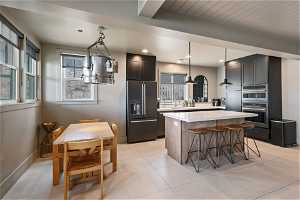 Kitchen featuring high end black refrigerator, light tile floors, a kitchen island, and decorative light fixtures